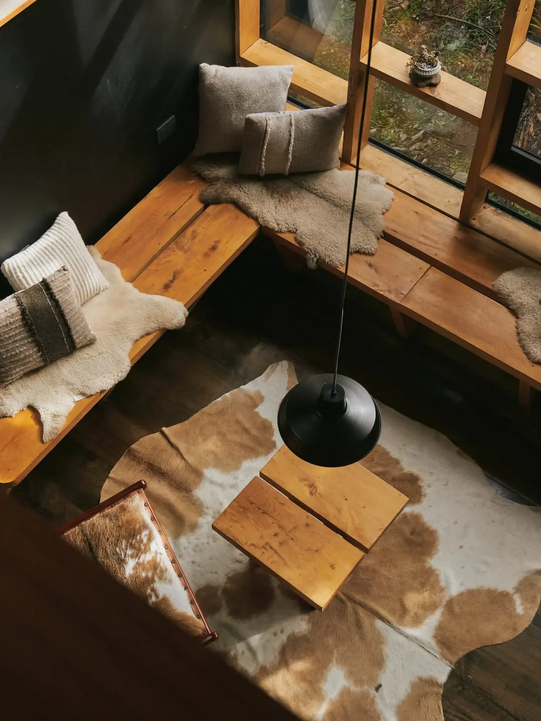 Rincón de lectura con bancas de madera, pieles y una lámpara colgante
