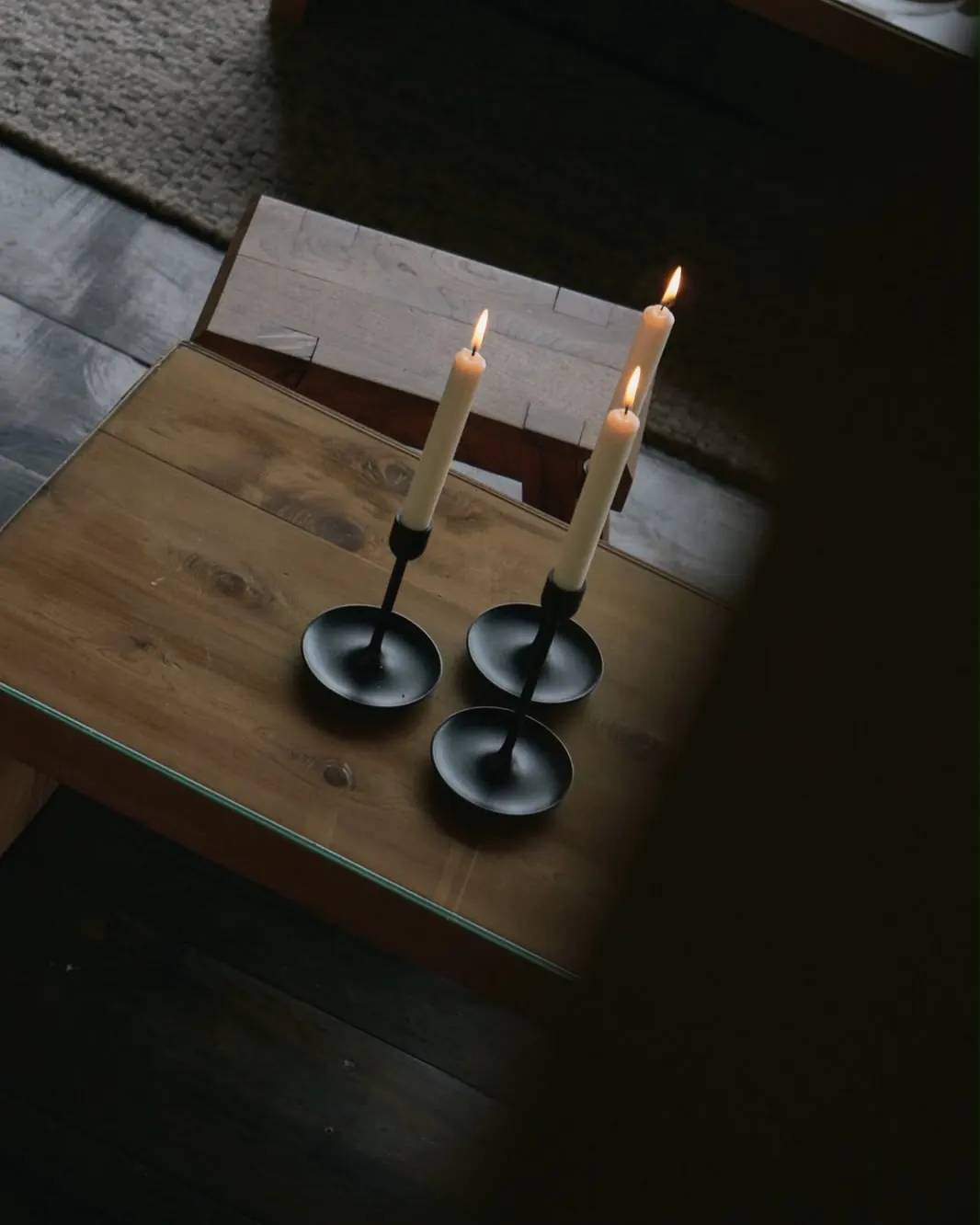 Dos velas encendidas en candelabros negros sobre madera