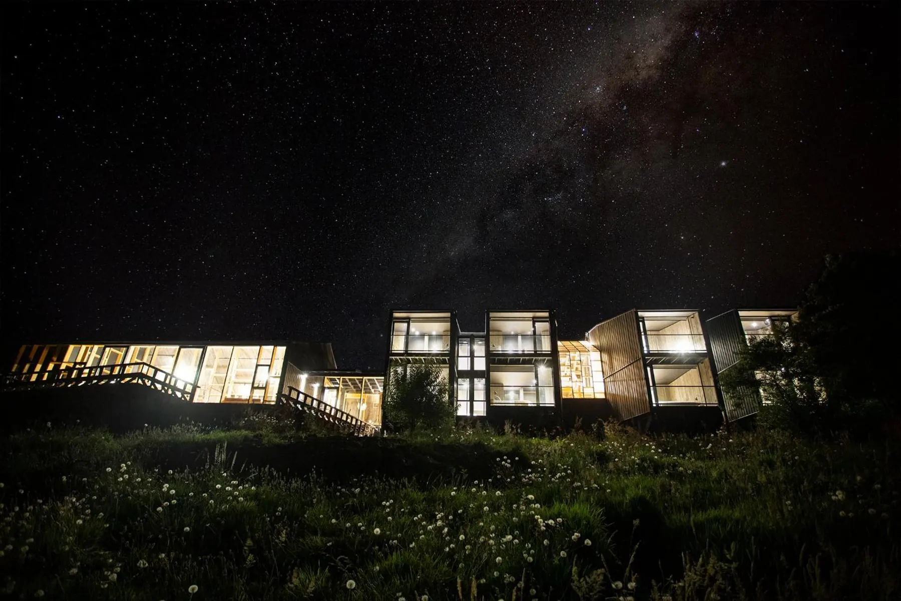 Los volúmenes de madera de RILÁN encendidos de noche bajo la Vía Láctea