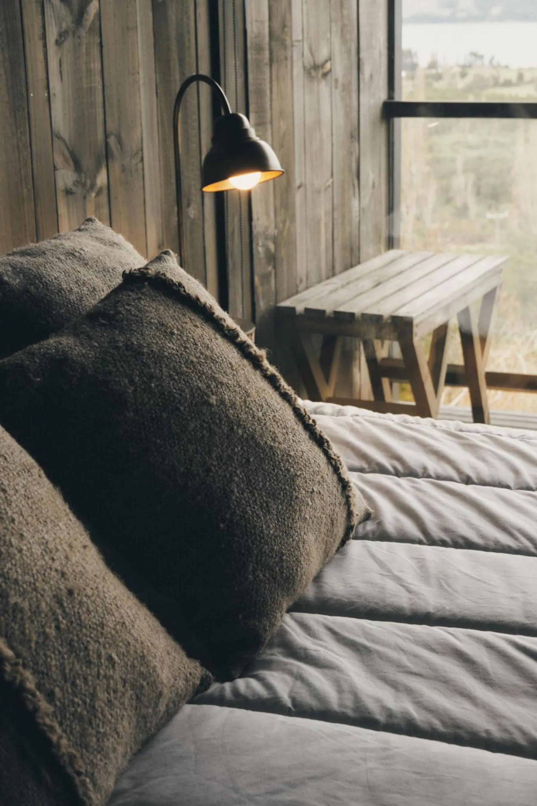 Cama con cojines de lana junto a una lámpara de lectura